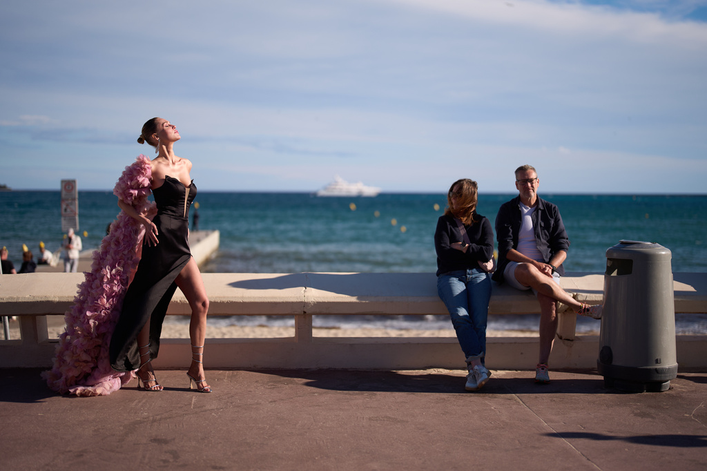 A festivalgoer poses for photographers as people sit by the beach along the Croisette during the 79th international film festival, Cannes, southern France, Friday, May 15, 2026. (AP Photo/John Locher)