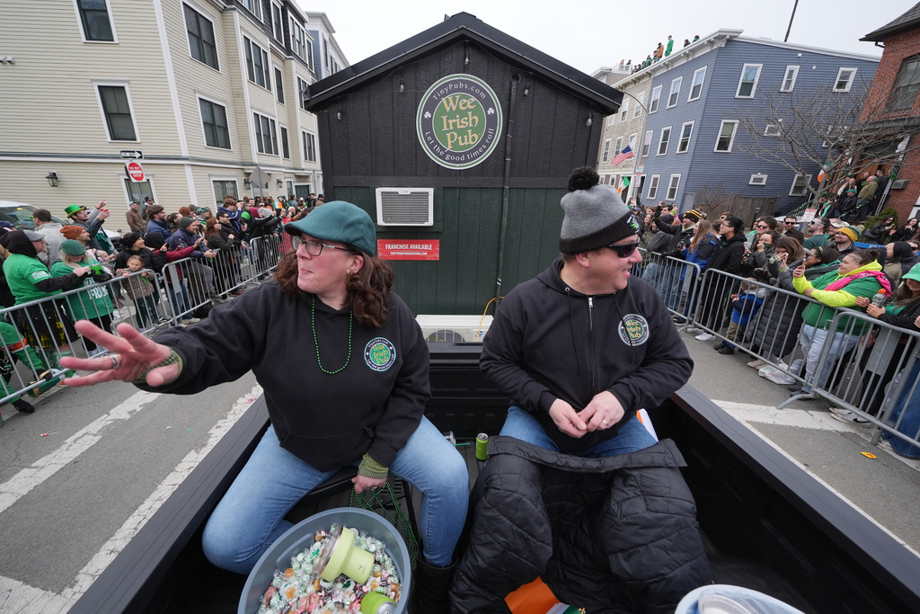 Dena Taylor, left, and Tony DiDonato toss candy to spectators while riding in a truck hauling the "Wee Irish Pub", a fully functioning mobile Irish pub built by two Massachusetts' brothers, during the annual St. Patrick's Day parade through the South Boston neighborhood, Sunday, March 15, 2026. (AP Photo/Charles Krupa)