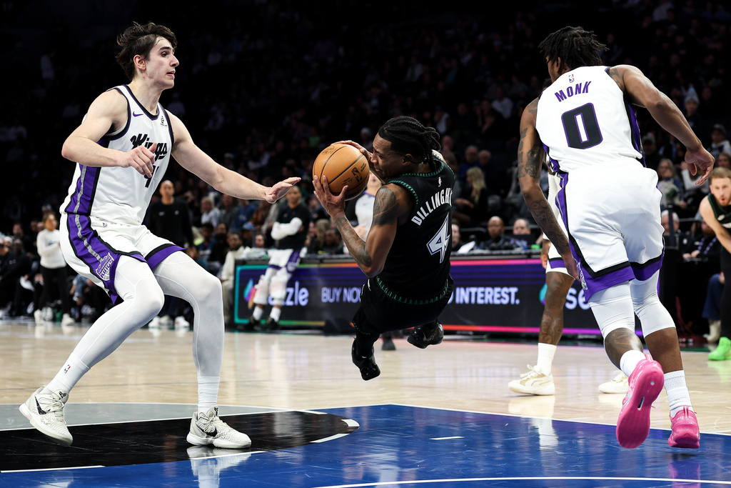 Minnesota Timberwolves guard Rob Dillingham, center, trips as he drives toward the basket while Sacramento Kings center Maxime Raynaud, left, and guard Malik Monk (0) defend during the first half of an NBA basketball game Sunday, Dec. 14, 2025, in Minneapolis. (AP Photo/Matt Krohn)
