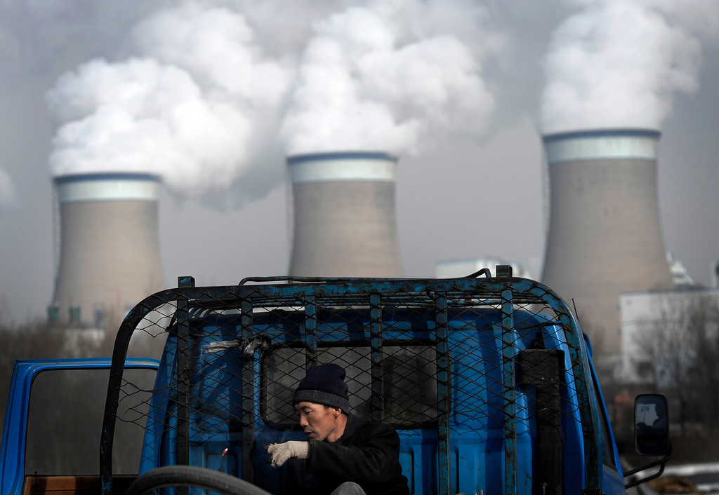 FILE - A worker throws his cigarette on a truck parked in front of a cooling towers of a coal-fired power plant in Dadong, Shanxi province, China, on Dec. 3, 2009. (AP Photo/Andy Wong, File)