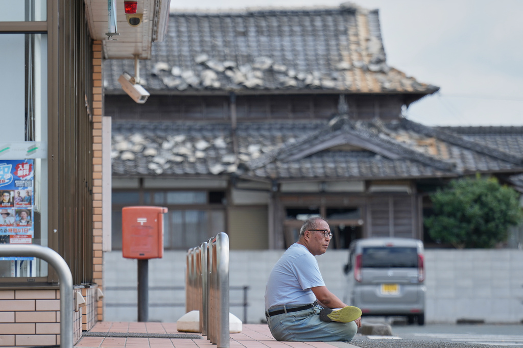 A person sits near a house damaged following an earthquake in Uki, Kumamoto Prefecture, southern Japan, Thursday, July 30, 2026. (AP Photo/Hiro Komae)