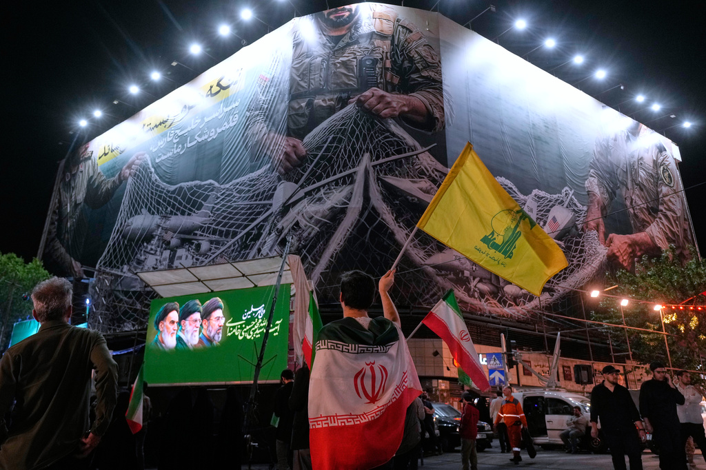 An Iranian demonstrator waves a flag of Lebanon's militant Hezbollah group under an anti-U.S. billboard depicting the American aircrafts into the Iranian armed forces fishing net with signs that read in Farsi: "The Strait of Hormuz will remain closed, The entire Persian Gulf is our hunting ground," during a pro-government gathering at Enqelab-e-Eslami, or Islamic Revolution, square in Tehran, Iran, Monday, May 4, 2026. (AP Photo/Vahid Salemi)