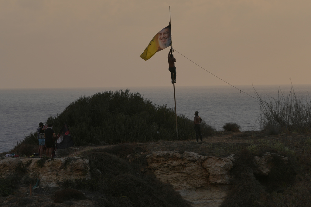 A Hezbollah supporter raises a flag with the portrait of late Hezbollah leader Sayyed Hassan Nasrallah, on the top of the landmark Raouche sea rock during an event commemorating the anniversary of his assassination, in Beirut, Lebanon, Thursday, Sept. 25, 2025. (AP Photo/Hussein Malla)