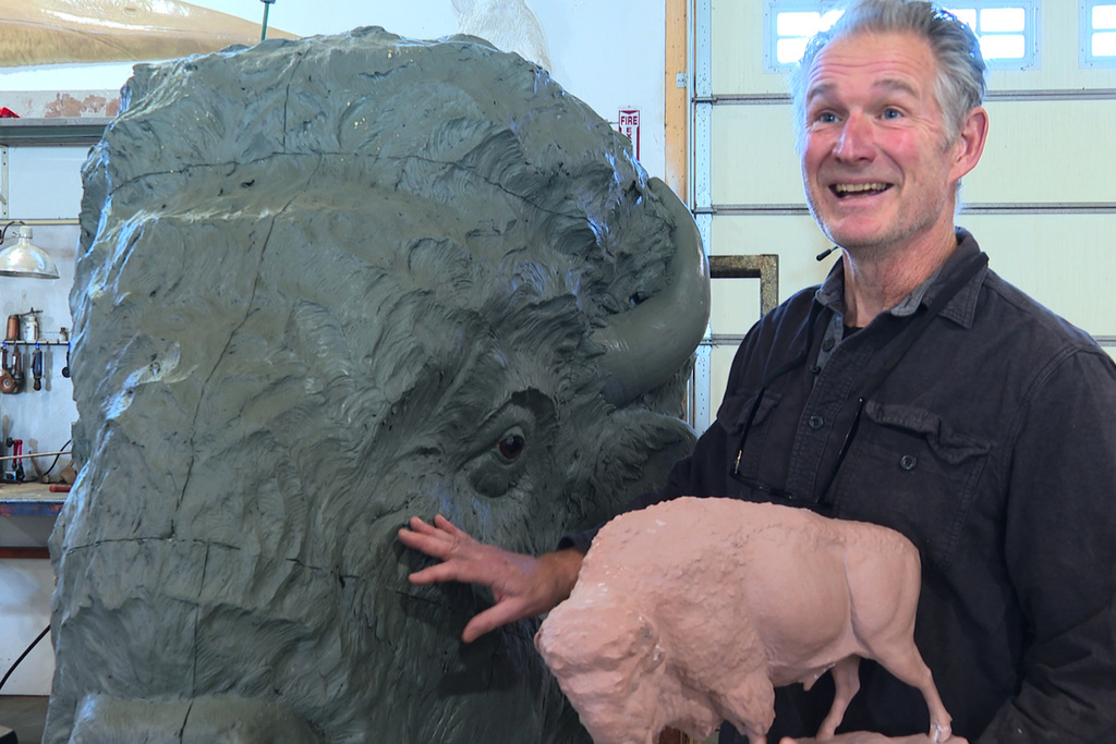 Paleoartist Gary Staab holds a small-scale prototype of a bison sculpture while standing next to the full-size clay sculpture he crafted at his studio in Kearney, Mo., on Tuesday, Dec. 2, 2025. (AP Photo/Nick Ingram)