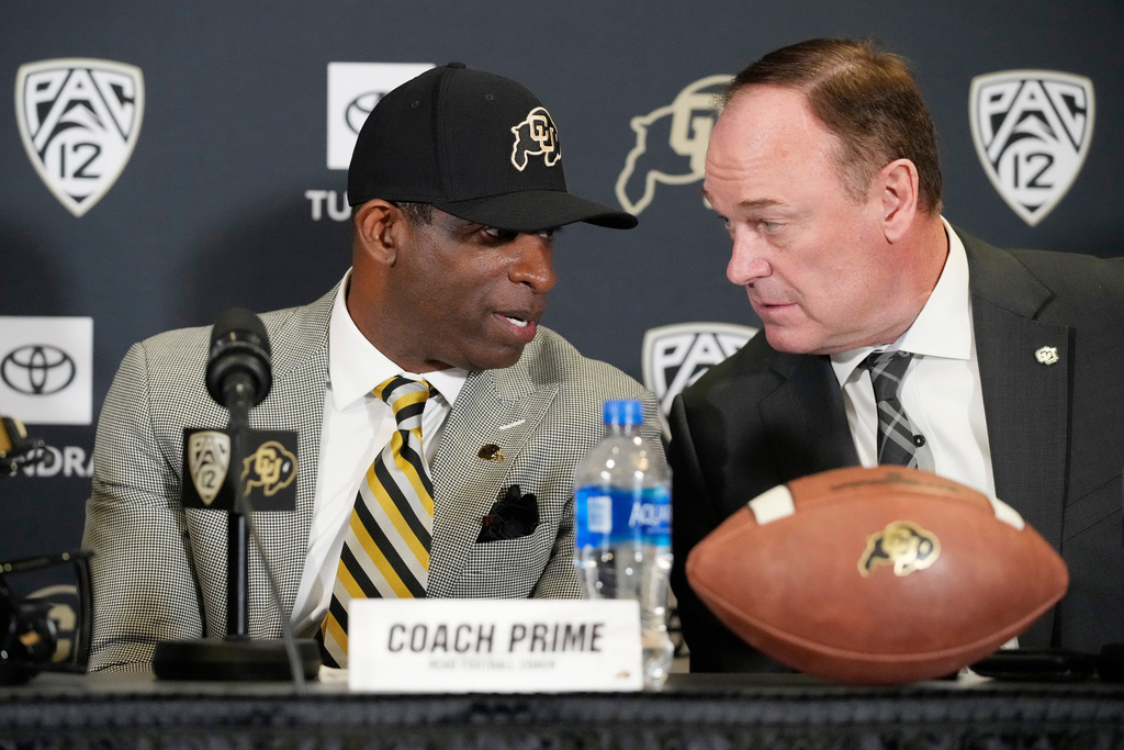 FILE- Deion Sanders, left, speaks with athletic director Rick George after Sanders was introduced as the new head football coach at the University of Colorado during a news conference Sunday, Dec. 4, 2022, in Boulder, Colo. (AP Photo/David Zalubowski, File)