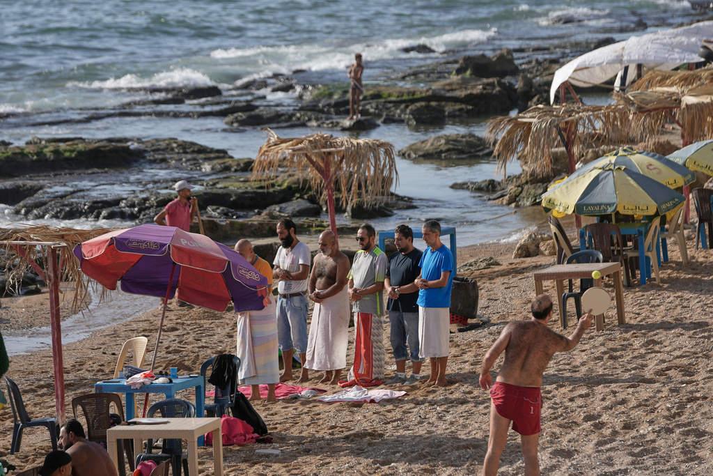 Syrian men attend their noon prayer, left, as others play racket ball at a public beach on the Mediterranean sea, in the coastal city of Latakia, Syria, Sunday, Oct. 5, 2025. (AP Photo/Hussein Malla)