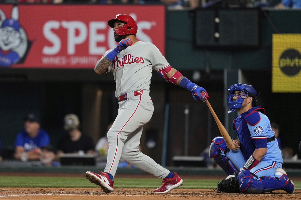 Philadelphia Phillies' Edmundo Sosa, left, follows through on a solo home run swing as Texas Rangers catcher Kyle Higashioka, right, looks on in the fifth inning of a baseball game Sunday, Aug. 10, 2025, in Arlington, Texas. (AP Photo/Tony Gutierrez)