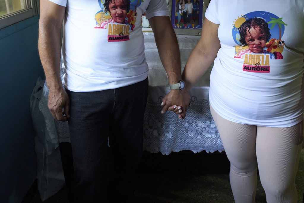 Married couple Syntia Caceres and Jose Martinez pose for photos wearing T-shirts with a photo of Aurore, Syntia's four-year-old granddaughter who was placed in foster care in Georgia state after her father, Caceres' son, was detained in July, at their home in Caracas, Venezuela, Thursday, 4, 2025. (AP Photo/Ariana Cubillos)