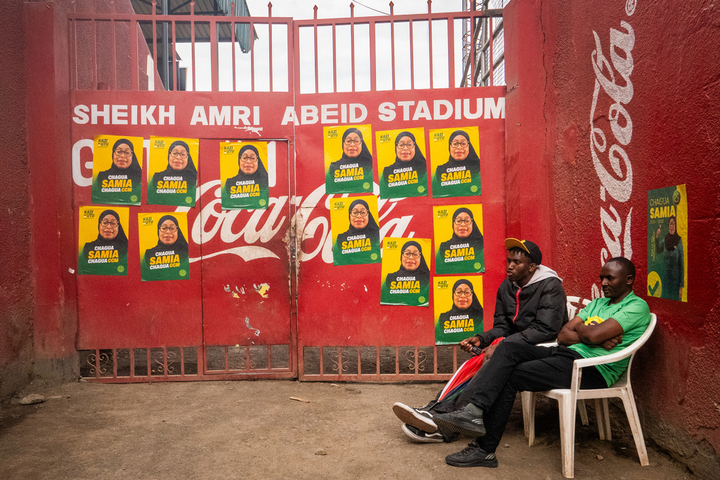 Men sit in front of campaign posters for Tanzanian presidential candidate Samia Suluhu Hassan, of the ruling Chama Cha Mapinduzi party, in Arusha, Tanzania, Oct. 8, 2025. (AP Photo)