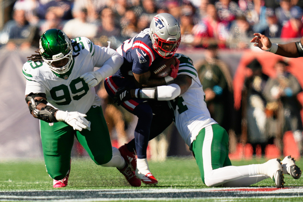 New York Jets defensive lineman T'vondre Sweat (99) and linebacker Jamien Sherwood, right, tackle New England Patriots running back Treveyon Henderson, center, during the first half of an NFL football game in Foxborough, Mass., Sunday, Oct. 18, 2026. (AP Photo/Charles Krupa)