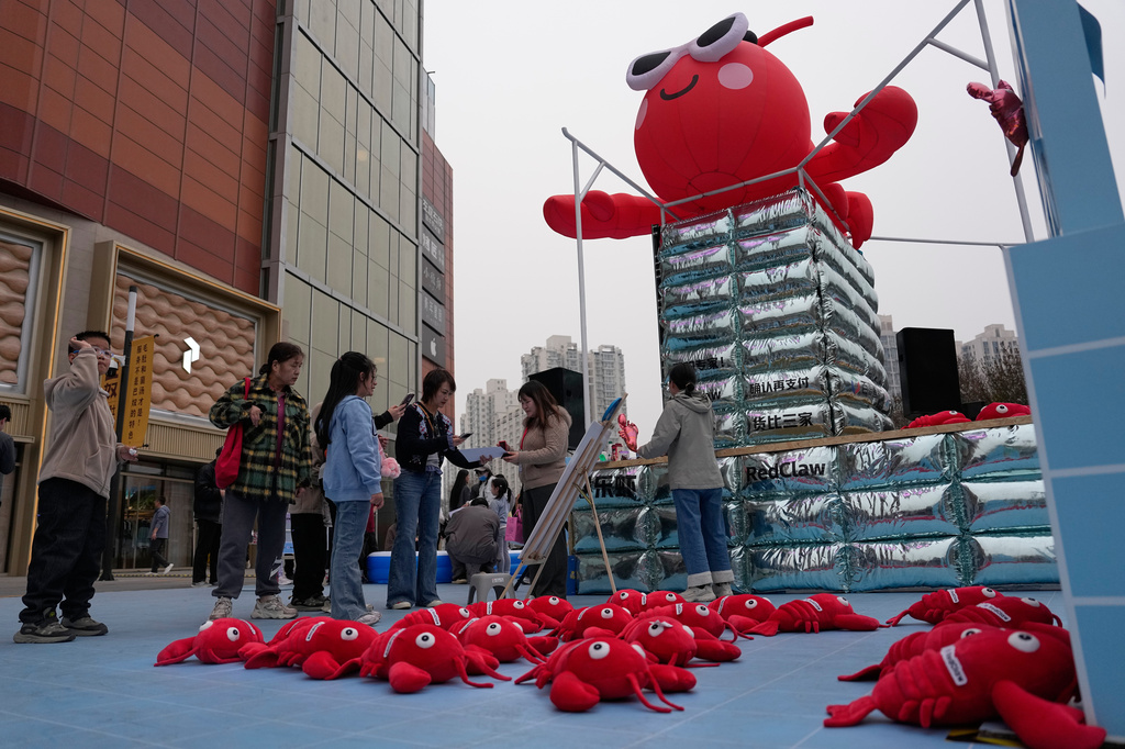 People play games at a RedClaw AI promotion booth set up outside a shopping mall in Beijing on March 28, 2026. (AP Photo/Andy Wong)