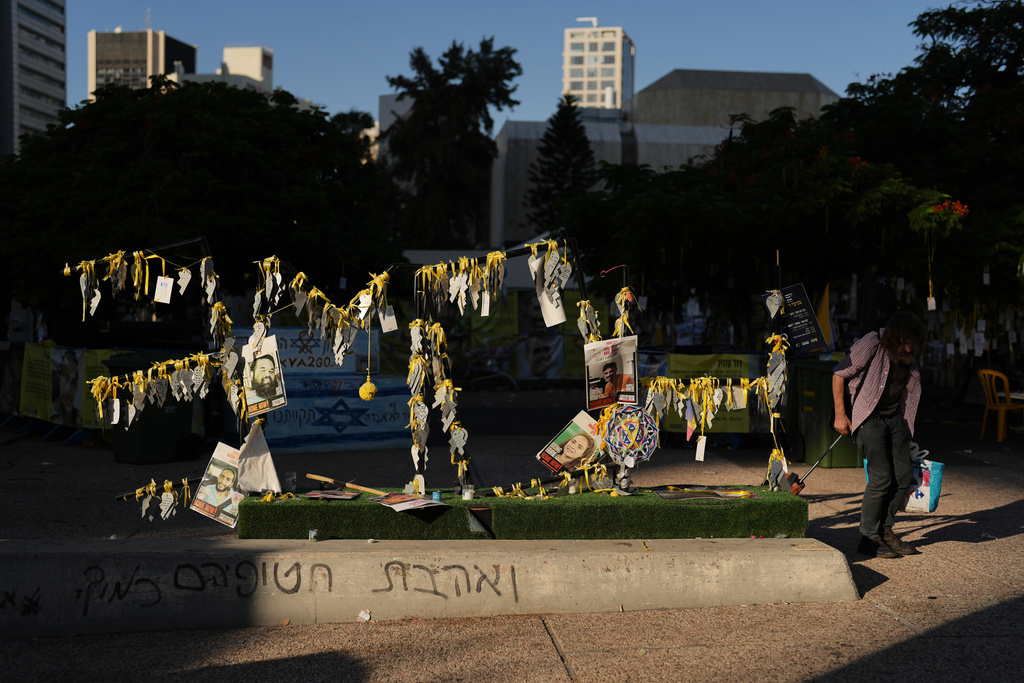 A man walks past photographs of Israeli hostages who were held by Hamas in the Gaza Strip, at the plaza known as hostages square, in Tel Aviv, Israel, Tuesday, Oct. 14, 2025. (AP Photo/Francisco Seco)