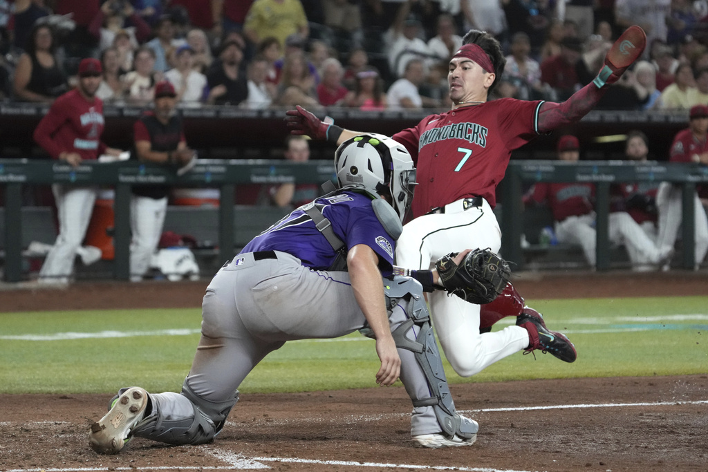Arizona Diamondbacks' Corbin Carroll, right, leaps to score against Colorado Rockies catcher Braxton Fulford, left, after a single hit by Ketel Marte in the fifth inning of a baseball game, Sunday, Aug 10, 2025, in Phoenix. (AP Photo/Rick Scuteri)