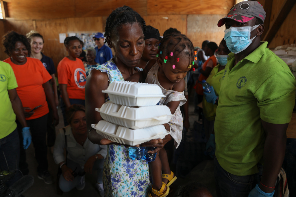 FILE - A woman carrying a child walks away with food from the World Food Program (WFP) at the Jean Marie Vincent High School whish has been turned into a shelter for families displaced by gang violence in the Tabarre neighborhood of Port-au-Prince, Haiti, Thursday, July 25, 2024. (AP Photo/Odelyn Joseph, File)