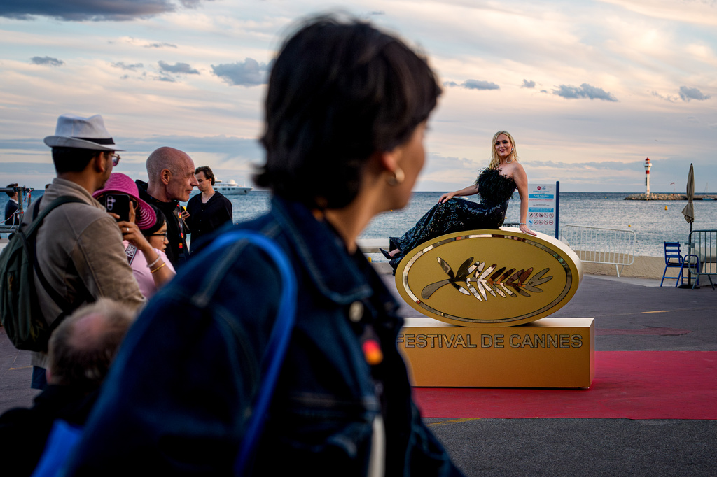 A woman poses for people on top of a sign of Festival de Cannes during the 79th international film festival, Cannes, southern France, Thursday, May 14, 2026. (AP Photo/Andreea Alexandru)
