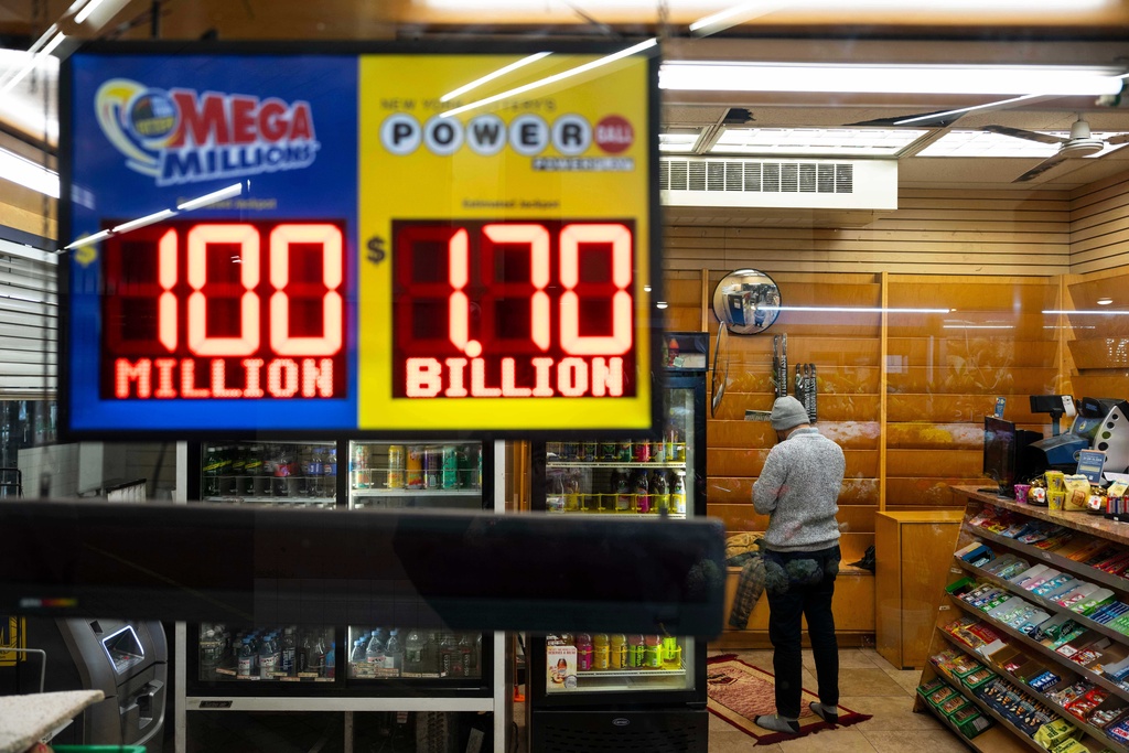 A convenience store employee prays while Jackpot payouts for Powerball and Mega Millions are displayed outside the store, Tuesday, Dec. 23, 2025, in New York. (AP Photo/Yuki Iwamura)