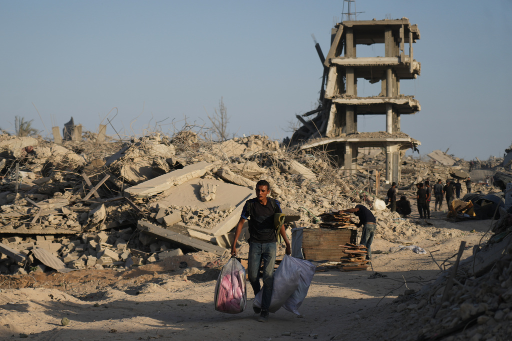 A displaced Palestinian man carries his belongings as he walks past destroyed buildings in the heavily damaged Sheikh Radwan neighborhood in Gaza City, Saturday, Oct. 11, 2025, after Israel and Hamas agreed to a pause in their war and the release of the remaining hostages. (AP Photo/Abdel Kareem Hana)