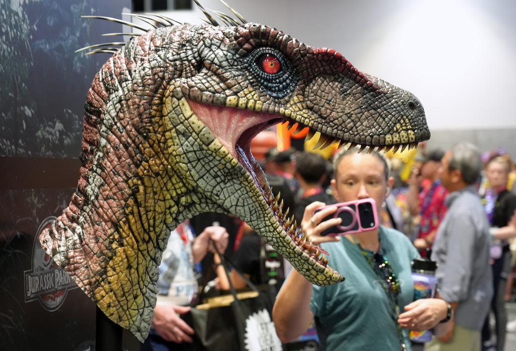 A Comic-Con attendee takes a cell phone picture of a bust of a male velociraptor from the film "Jurassic Park III" at the Elite Creature Collectibles booth during preview night at Comic-Con International on Wednesday, July 22, 2026, in San Diego. (AP Photo/Chris Pizzello)