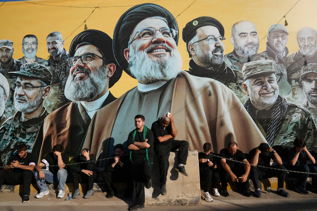 Hezbollah supporters sit in front of a giant billboard, that shows the two late hezbollah leaders Sayyed Hassan Nasrallah and Hashem Safieddine, centre, with other Hezbollah killed commanders, as they listen to the death story of Imam Hussein during the holy day of Ashoura in Dahiyeh, Beirut's southern suburbs, Lebanon, Friday, June 26, 2026. (AP Photo/Hussein Malla)