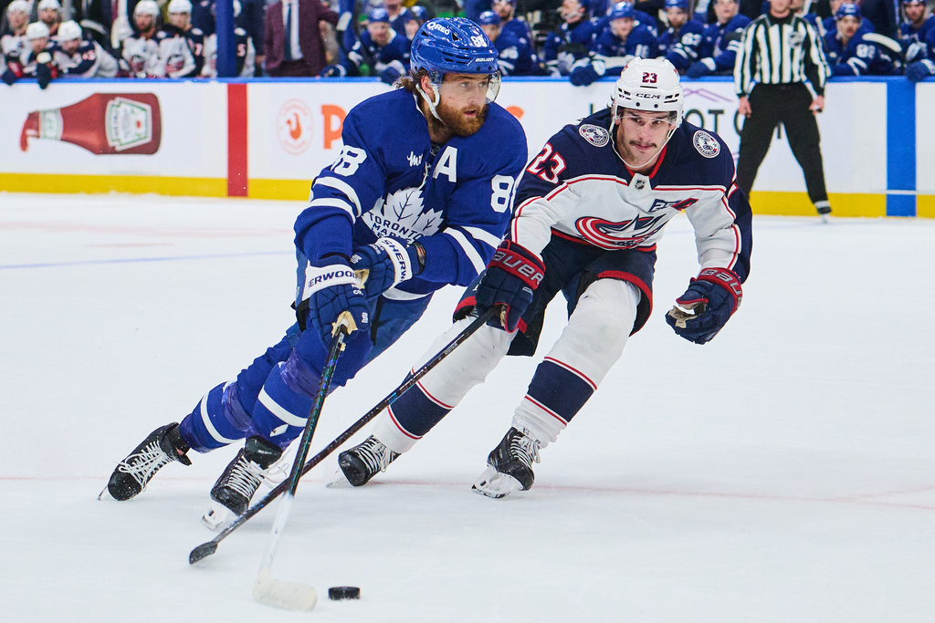 Toronto Maple Leafs' William Nylander (88) and Columbus Blue Jackets' Sean Monahan (23) battle for the puck during overtime NHL hockey action in Toronto, on Thursday, Nov. 20, 2025. (Sammy Kogan/The Canadian Press via AP)