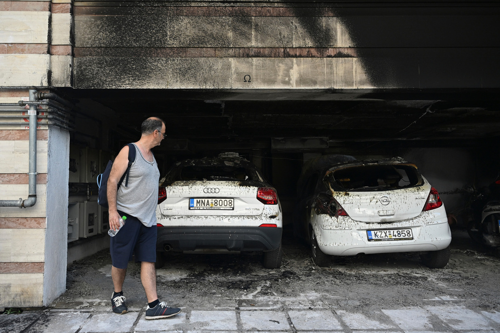 A man looks at burned vehicles following firebomb attacks that apparently targeted members of Greece's governing conservative New Democracy party in the northern port city of Thessaloniki, Greece, Wednesday, July 1, 2026. (AP Photo/Giannis Papanikos)