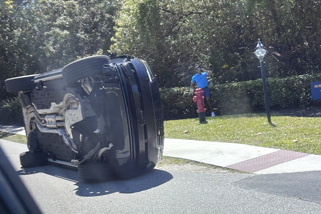 Golfer Tiger Woods stands by his overturned vehicle in Jupiter Island, Fla., on Friday, March 27, 2026. (AP Photo/Jason Oteri)