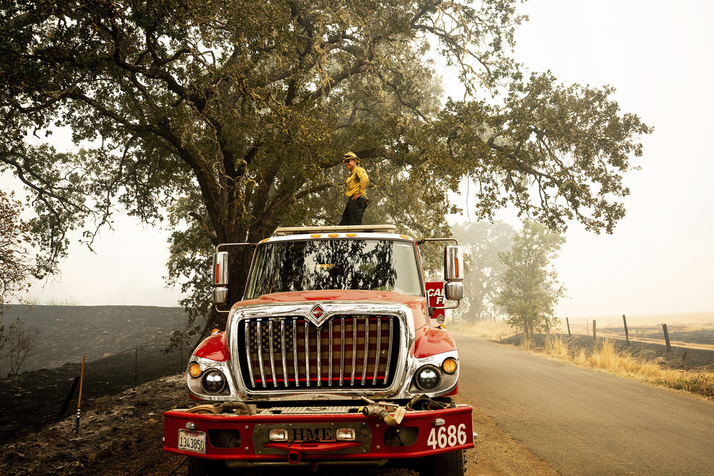A firefighter stands atop a truck while battling the Pickett Fire burning in the Aetna Springs area of Napa County, Calif., on Sunday, Aug. 24, 2025. (AP Photo/Noah Berger)