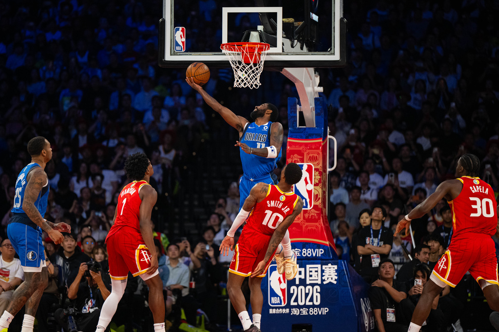 In this photo released by Xinhua News Agency, Kyrie Irving of the Dallas Mavericks, center top, attempts a shot during a preseason NBA basketball game against the Houston Rockets, in Macao on Sunday, Oct. 11, 2026. (Cheong Kam Ka/Xinhua via AP)