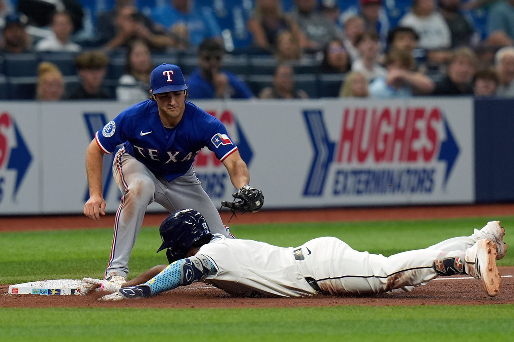 Tampa Bay Rays' Junior Caminero slides into third base with a triple ahead of the tag by Texas Rangers' Josh Smith during the sixth inning of a baseball game Tuesday, July 28, 2026, in St. Petersburg, Fla. (AP Photo/Chris O'Meara)
