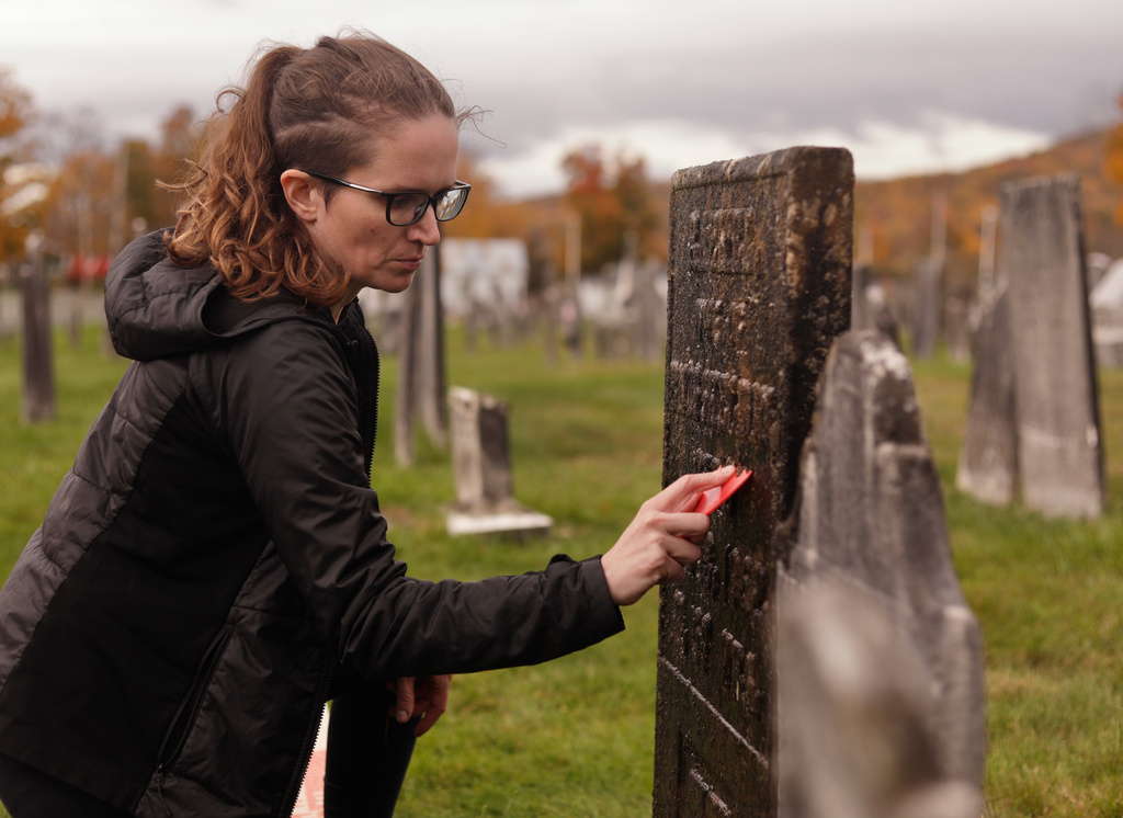 Caitlin Abrams, who became popular on TikTok for her grave cleaning videos, scrapes away moss and lichen from a gravestone at a cemetery in Rupert, Vt., Wednesday, Oct. 14, 2026. (AP Photo/Amanda Swinhart)