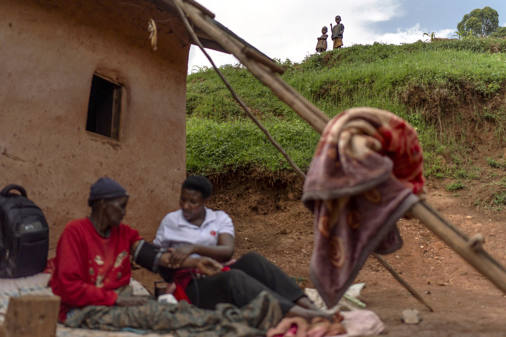 Young children look on as their grandmother, Prasidia Tishwekwa, who is in her 80s, has her blood pressure checked by field nurse Winnie Katwesigye outside their home Wednesday, Nov. 20, 2024, in Rutarabana, a rural village in western Uganda. (AP Photo/David Goldman)
