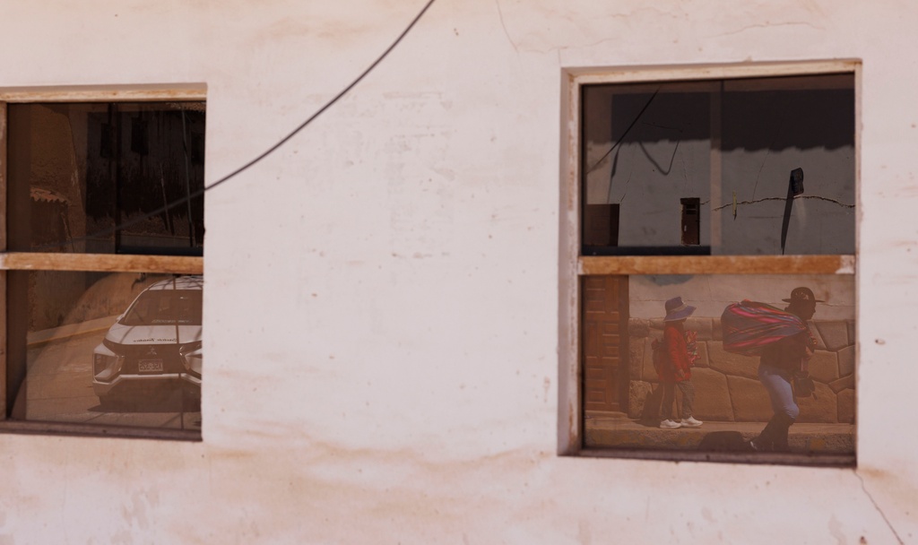 People walk down the street, one with a pack made of textiles over their shoulder, in the Chincheros region of the Sacred Valley, Peru, on Saturday, Aug. 30, 2025. (AP Photo/Alie Skowronski)
