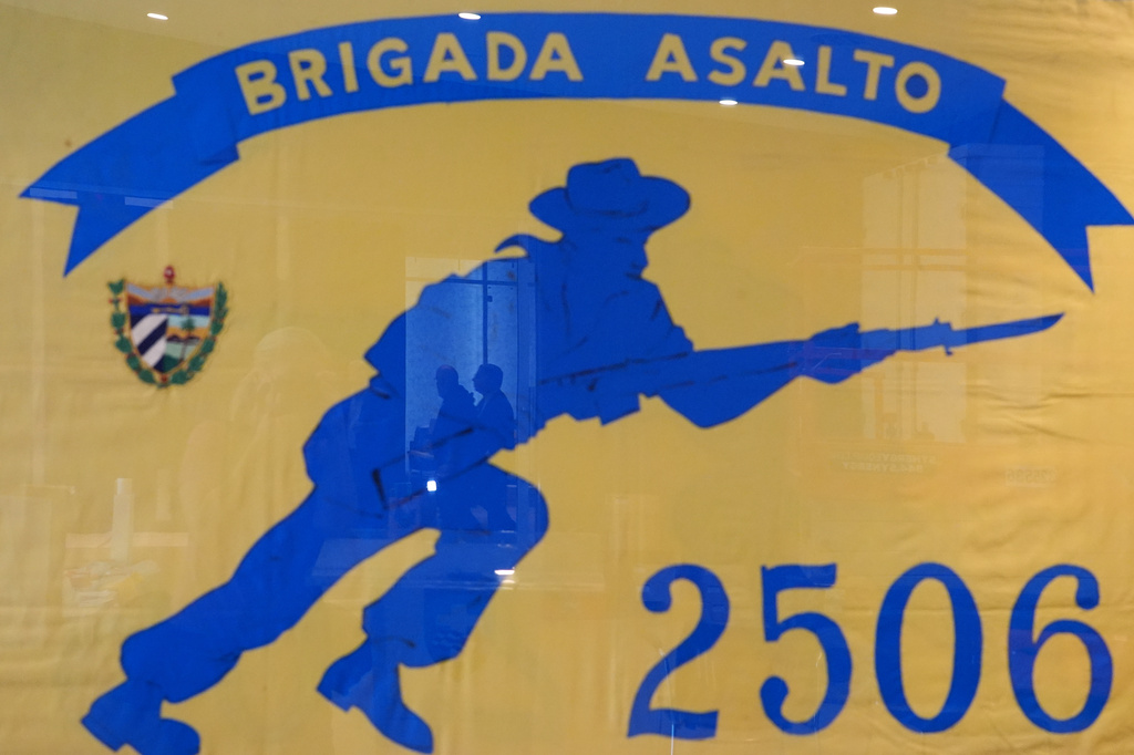 People are reflected in a framed Brigade 2506 flag, as preparation work continues for the reopening of the Bay of Pigs Museum in a new and expanded space in Miami's Little Havana neighborhood, Tuesday, April 7, 2026. (AP Photo/Rebecca Blackwell)