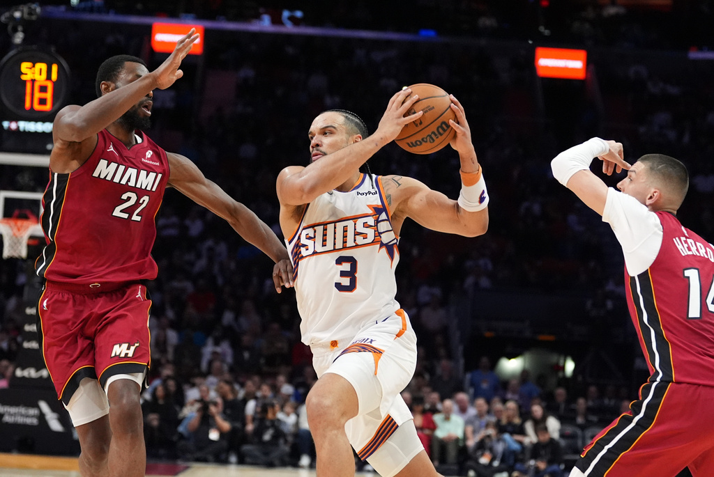 Phoenix Suns guard/forward Dillon Brooks (3) drives forward defended by Miami Heat forward Andrew Wiggins (22) and guard Tyler Herro (14) during the first half of an NBA basketball game, Tuesday, Jan. 13, 2026, in Miami. (AP Photo/Rebecca Blackwell)