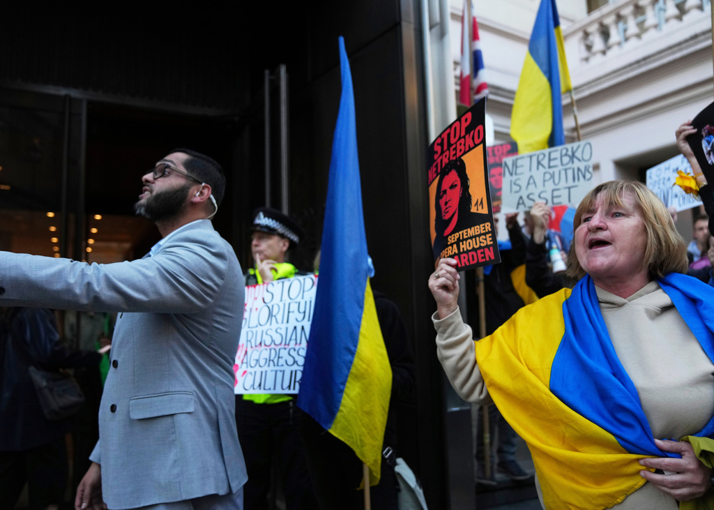Pro-Ukraine protesters hold up placards and flags during a demonstration against the Royal Opera House in London, as the house had set an Russian opera singer to perform the lead in Puccini's Tosca, Thursday, Sept. 11, 2025. (AP Photo/Joanna Chan)