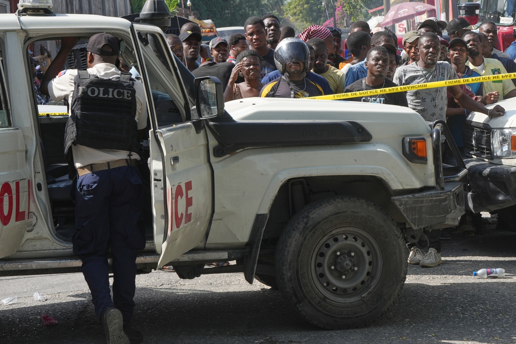 People watch police work a crime scene after a foiled attempted kidnapping in the Delmas district of Port-au-Prince, Haiti, Monday, Feb. 23, 2026. (AP Photo/Odelyn Joseph)