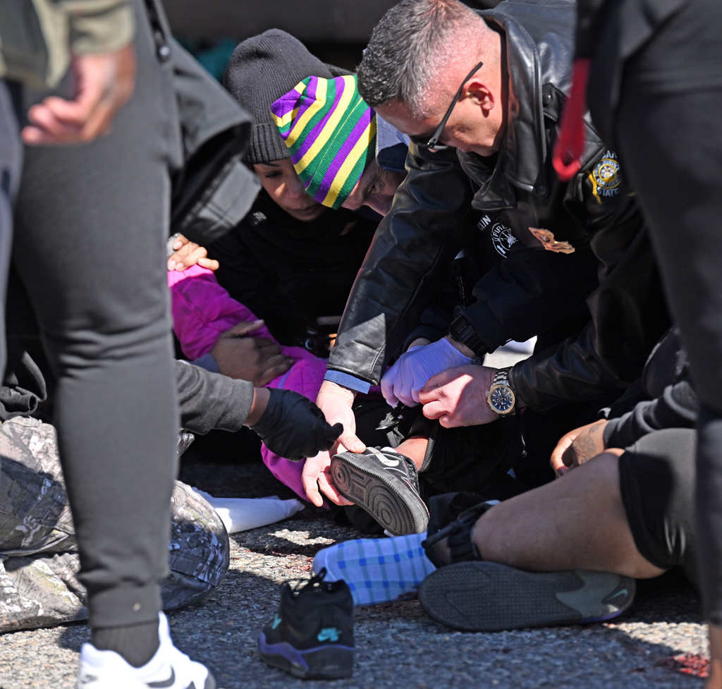 A Louisiana State Trooper removes the shoe of a young shooting victim as law enforcement personnel work at the scene of a shooting at the Clinton Mardi Gras Parade in Baton Rouge, La., on Saturday, Jan. 31, 2026. (Hilary Scheinuk/The Advocate via AP)