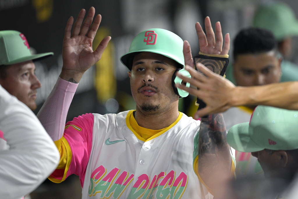 San Diego Padres' Manny Machado, center, is congratulated in the dugout after scoring on a sacrifice fly hit by Xander Bogaerts during the fourth inning of a baseball game against the Los Angeles Dodgers, Friday, Aug. 22, 2025, in San Diego. (AP Photo/Orlando Ramirez)