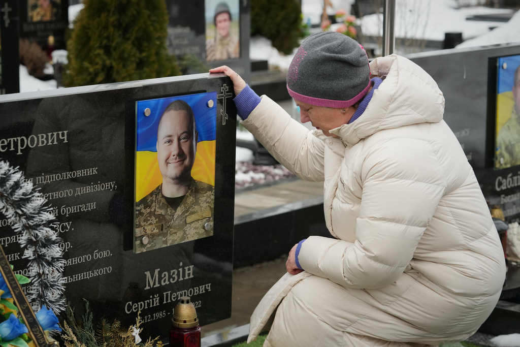 A woman sits in front of a grave of her relative during memorial service for fallen Ukrainian soldiers during a ceremony to mark the fourth anniversary of the Russian invasion of Ukraine, in Bucha, Ukraine, Tuesday, Feb. 24, 2026. (AP Photo/Sergei Grits)