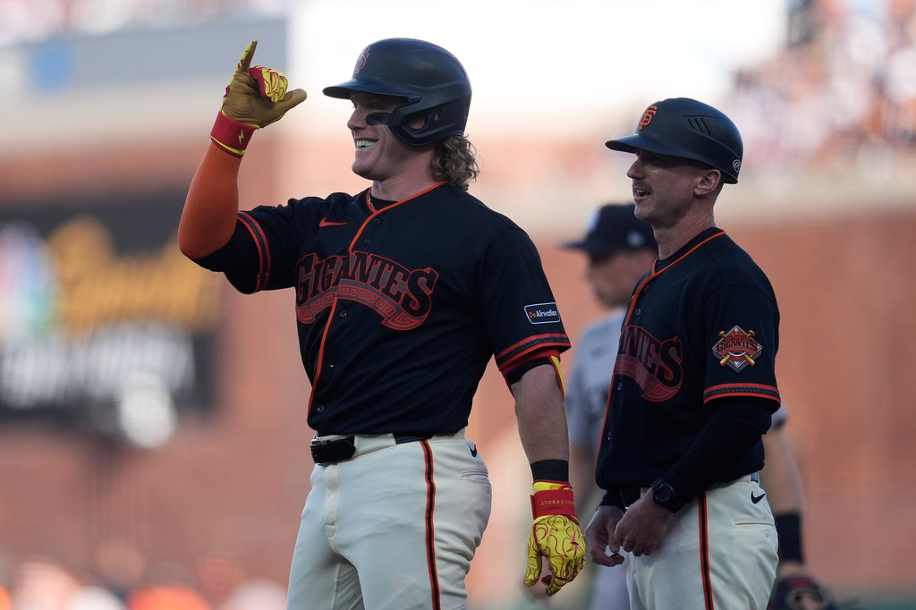 San Francisco Giants' Harrison Bader, left, gestures toward teammates after hitting a single next to first base coach Shane Robinson during the fourth inning of a baseball game against the New York Yankees in San Francisco, Saturday, March 28, 2026. (AP Photo/Jeff Chiu)