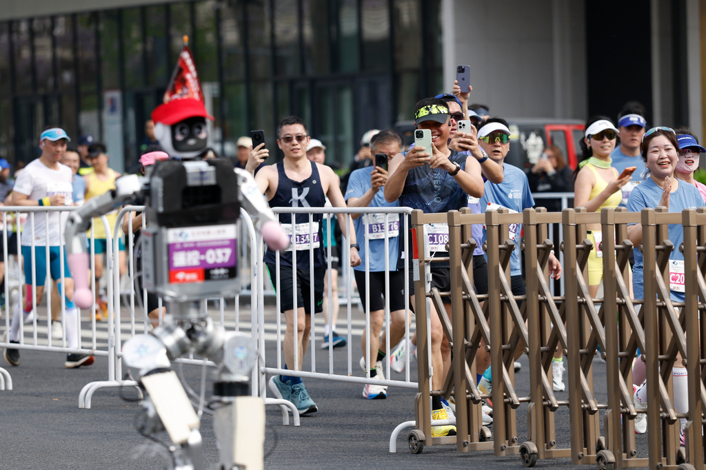Runners take pictures of a humanoid robot in the second Beijing E-Town Half Marathon and Humanoid Robot Half Marathon in Beijing Sunday, April 19, 2026. (Haruna Furuhashi/Pool Photo via AP)