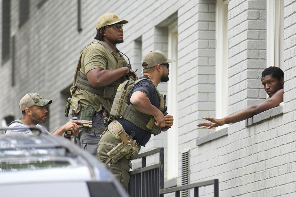 Armed officers prepare to place handcuffs on a man from within an apartment complex, Tuesday, Aug. 19, 2025, in the Petworth neighborhood of northwest Washington. The officers pictured had "Washington Field Office" on their shirts underneath tactical gear that said Police. (AP Photo/Jacquelyn Martin)