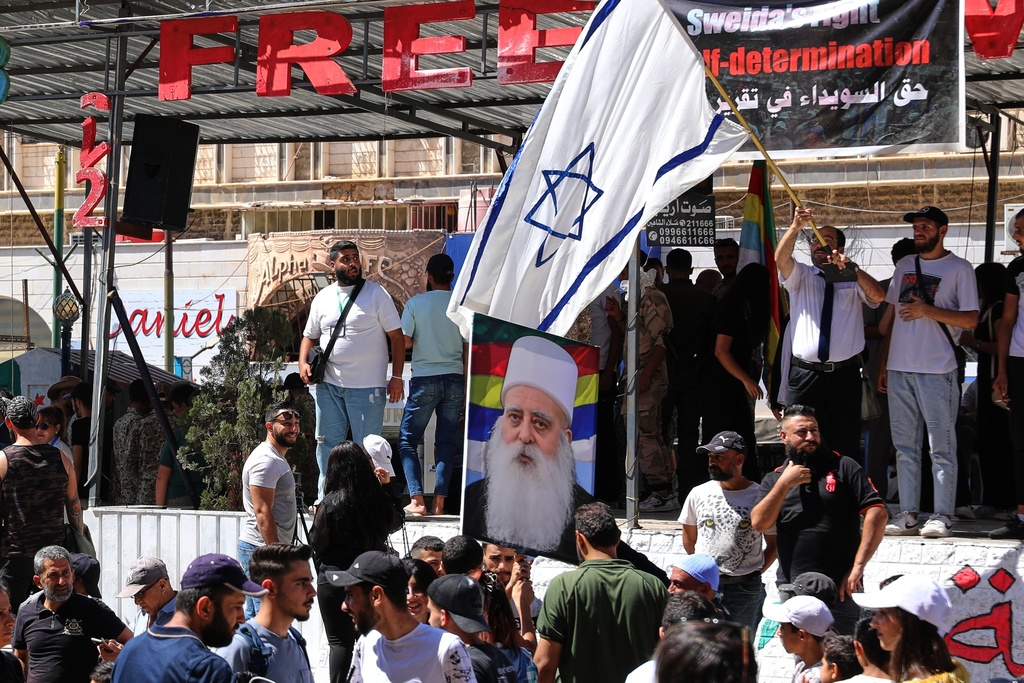 A man waves an Israeli flag over a picture of Sheikh Mowafak Tarif, the spiritual leader of the Druze in Israel, during a weekly rally in Sweida, southern Syria, on Sept. 20, 2025. (AP Photo/Fahd Kiwan)