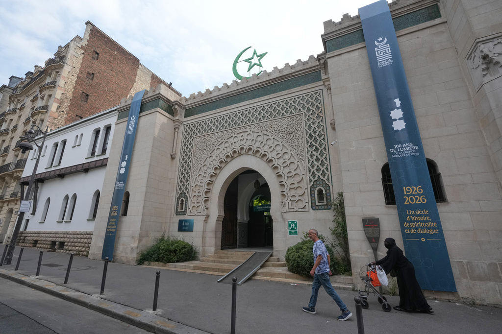 People walk past the Grand Mosque of Paris, where a banner reads, "100 years of light, a century of history, spirituality and dialogue" marking its 100th anniversary, Friday, July 17, 2026. (AP Photo/Michel Euler)
