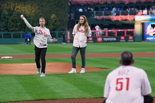 CORRECTS FIRST NAME TO RYAN, NOT MATT - Braden Halladay, left, accompanied by his brother Ryan Halladay, throws a ceremonially first pitch to former Philadelphia Phillies catcher Carlos Ruiz, marking the 15th anniversary of their father Roy Halladay's postseason no-hitter, ahead of Game 2 of baseball's National League Division Series between the Phillies and the Los Angeles Dodgers, Monday, Oct. 6, 2025, in Philadelphia. (AP Photo/Matt Rourke) CORRECTS FIRST NAME TO RYAN, NOT MATT - Braden Halladay, left, accompanied by his brother Ryan Halladay, throws a ceremonially first pitch to former Philadelphia Phillies catcher Carlos Ruiz, marking the 15th anniversary of their father Roy Halladay's postseason no-hitter, ahead of Game 2 of baseball's National League Division Series between the Phillies and the Los Angeles Dodgers, Monday, Oct. 6, 2025, in Philadelphia. (AP Photo/Matt Rourke)