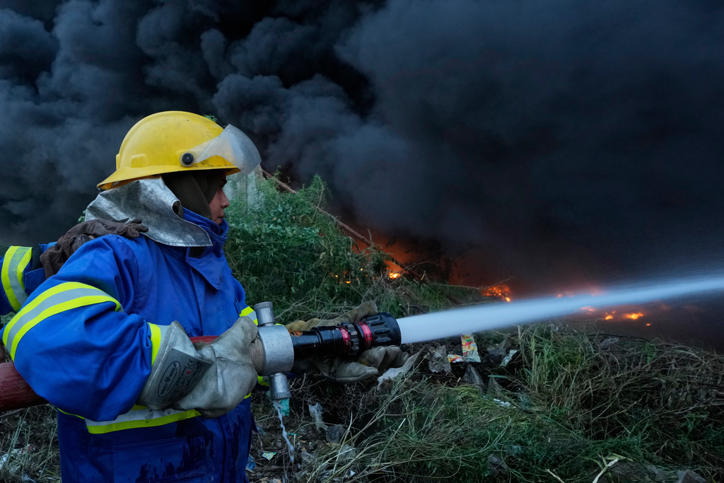 Female firefighter Syeda Masooma Zaidi sprays water to extinguish on a fire broke out in a storage facility packed vehicles tires, outskirts of Karachi, Pakistan, Thursday, Oct. 30, 2025. (AP Photo/Fareed Khan)