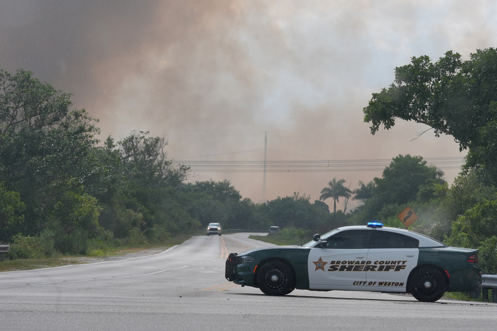 A Broward County Sheriff's police car blocks the entrance to a park as a wildlife burns in Broward County, Fla., Monday, May 11, 2026. (AP Photo/Marta Lavandier)
