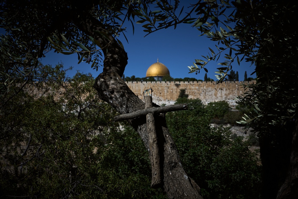 A cross hangs from an olive tree in the Franciscan hermitage on the Mount of Olives with the Dome of the Rock shrine at the Al-Aqsa Mosque compound in the background, in Jerusalem, Friday, Oct. 3, 2025. (AP Photo/Oded Balilty)