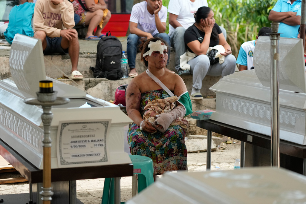 Earthquake survivor Jesiel Malinao sits beside the coffins of her two sons on Thursday, Oct. 2, 2025 after a strong earthquake on Tuesday caused a landslide that toppled their hillside homes in Bogo city, Cebu Province, Central Philippines. (AP Photo/Aaron Favila)
