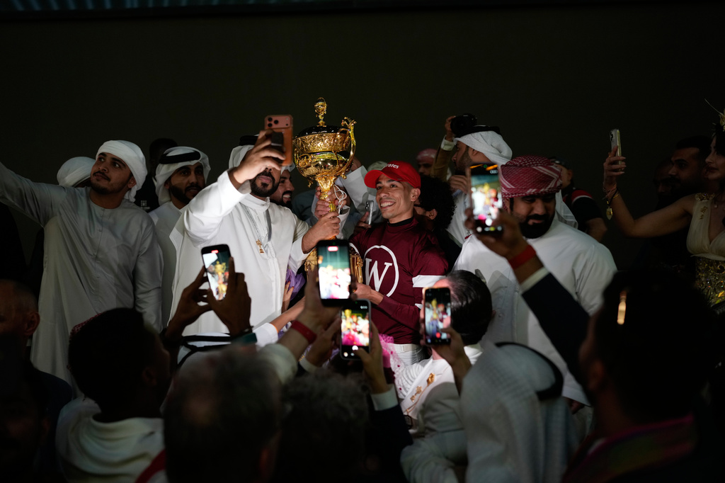 Magnitude's jockey Jose Ortiz, center, poses for photos while holding the trophy after winning the $12 million Dubai World Cup horse race over 2,000 meters (10 furlongs) at Meydan Racecourse in Dubai, United Arab Emirates, Saturday, March 28, 2026. (AP Photo/Altaf Qadri)